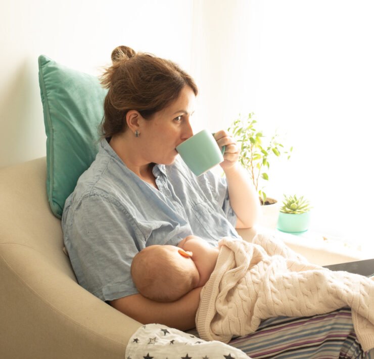 młoda mama karmi dziecko piersią i pije kawę