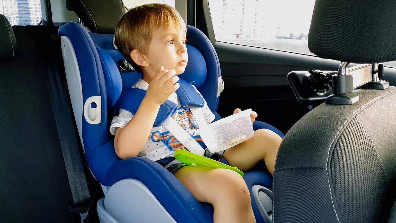 dziecko w foteliku samochodowym je zdrową przekąskę w podróży