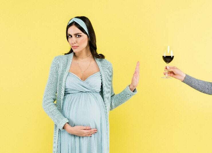 kobieta w ciąży na żółtym tle odmawia lampki wina