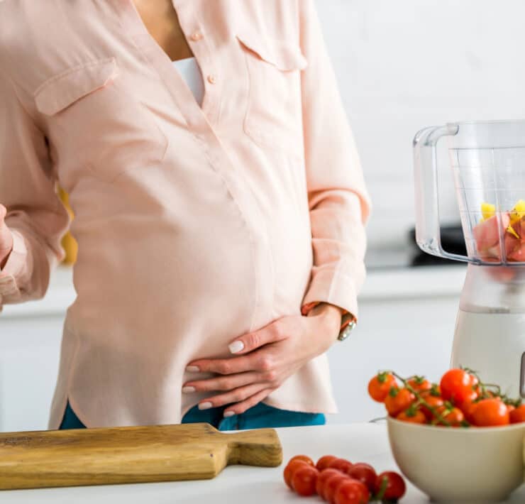 kobieta w ciąży trzyma się za brzuch, w drugiej ręce trzyma sok pomidorowy