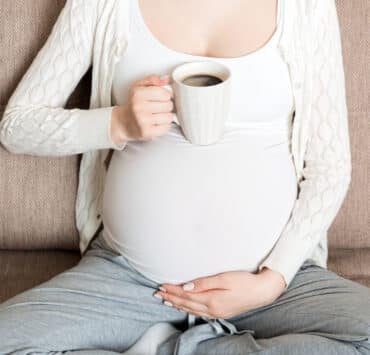 kobieta w ciąży z kubkiem czarnej kawy w ręku