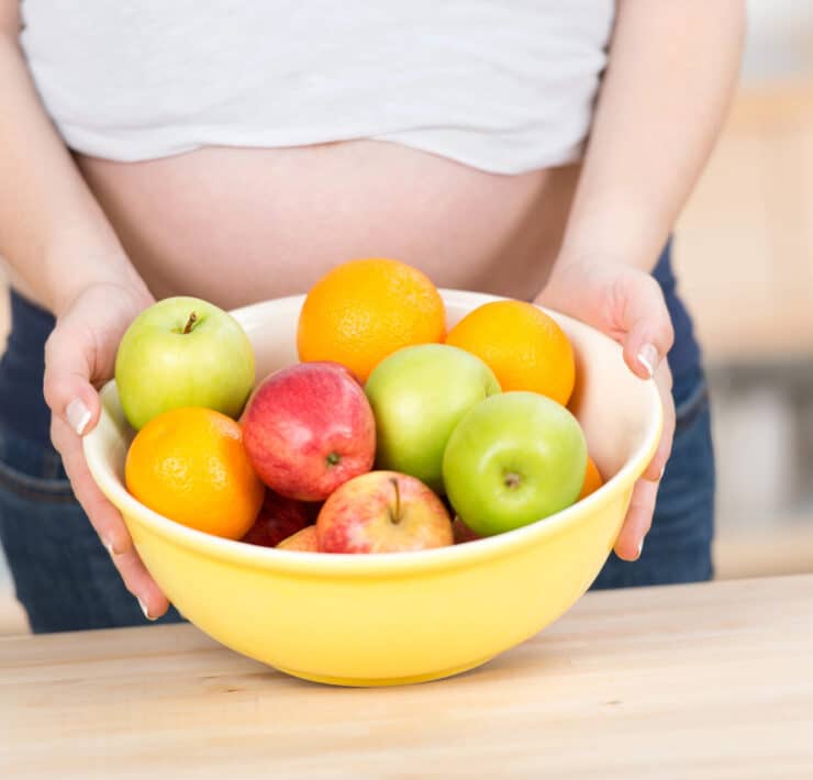 kobieta w ciąży z miską owoców: jabłek i pomarańczy