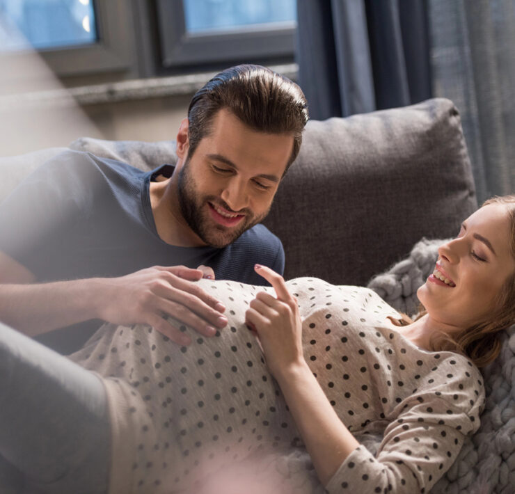 Szczęśliwa para oczekująca dziecka. Kobieta leży na kanapie, a mężczyzna delikatnie dotyka jej brzucha.
