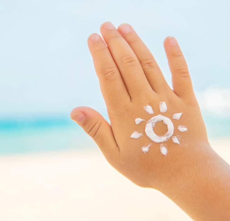 Dłoń dziecka z narysowanym kremem z filtrem przeciwsłonecznym słońcem – ochrona skóry przed słońcem na plaży.