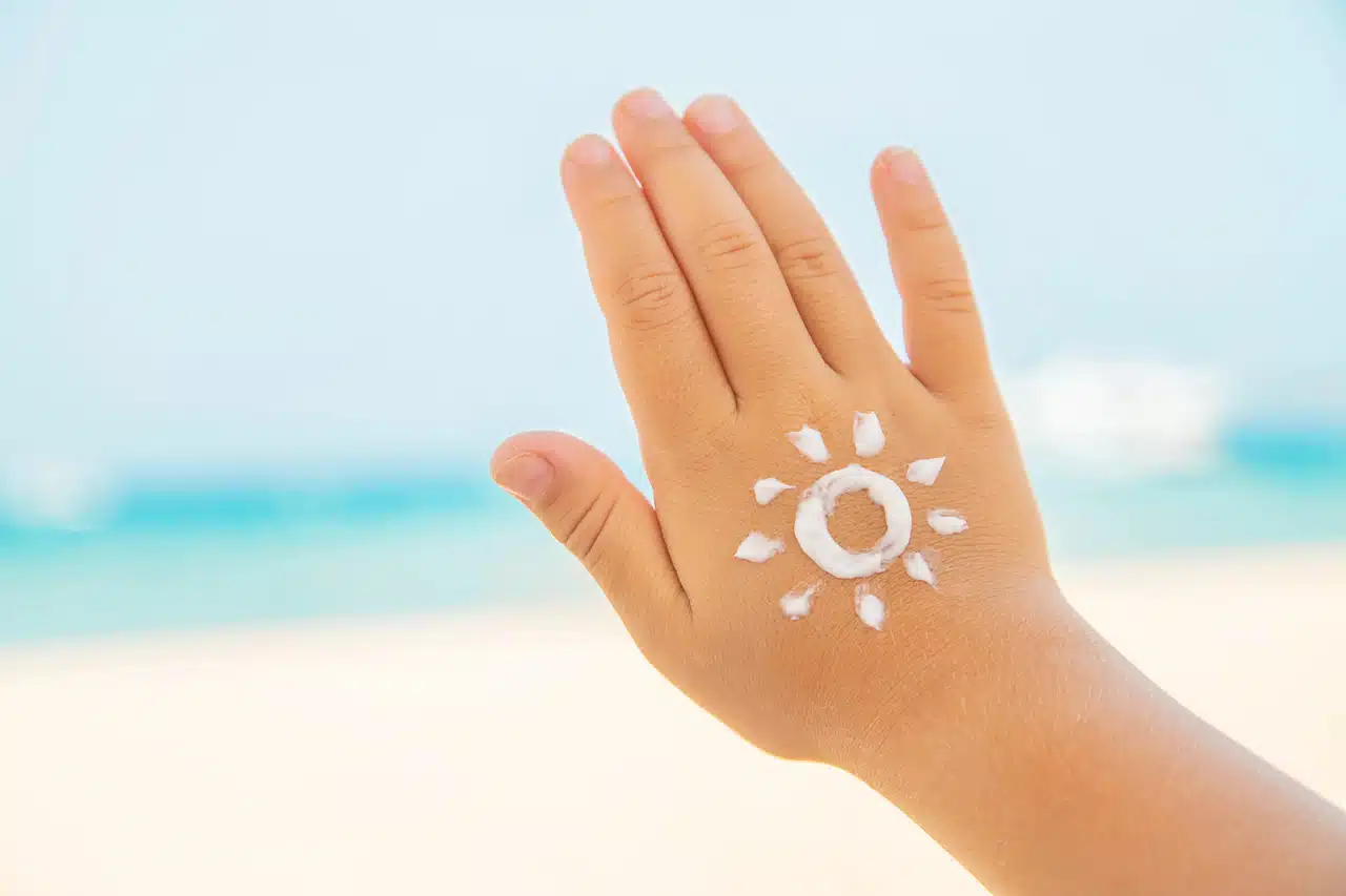 Dłoń dziecka z narysowanym kremem z filtrem przeciwsłonecznym słońcem – ochrona skóry przed słońcem na plaży.