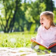 wesoła dziewczynka czyta książkę na wakacje na łące