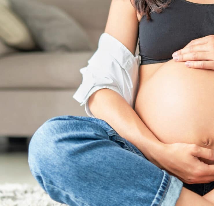 Ciężarna kobieta siedząca na podłodze, trzymająca dłonie na brzuchu – ilustracja artykułu o L4 w ciąży i prawach przyszłych mam