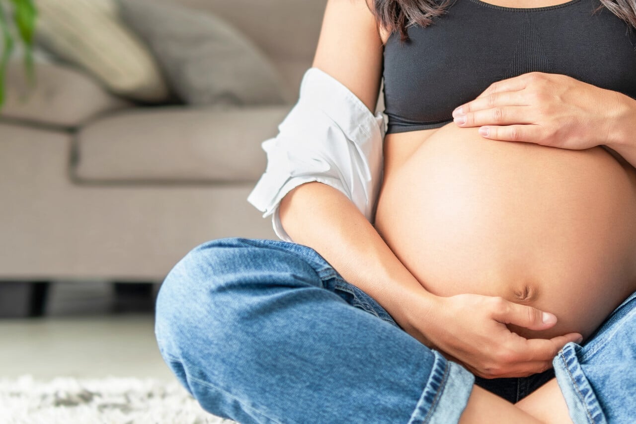 Ciężarna kobieta siedząca na podłodze, trzymająca dłonie na brzuchu – ilustracja artykułu o L4 w ciąży i prawach przyszłych mam