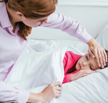 mama trzyma rękę na czole dziecka i mierzy jej temperaturę przy stanie podgorączkowym