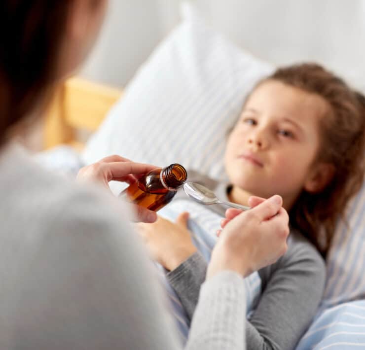 mama, której przyznano zasiłek opiekuńczy na dziecko podaje córce leki w czasie choroby