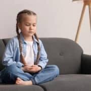 dziewczynka siedzi z zamkniętymi oczami i ćwiczy uważny oddech