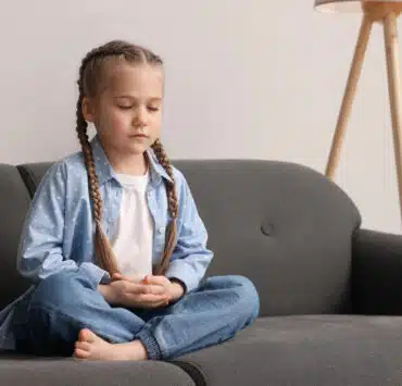 dziewczynka siedzi z zamkniętymi oczami i ćwiczy uważny oddech