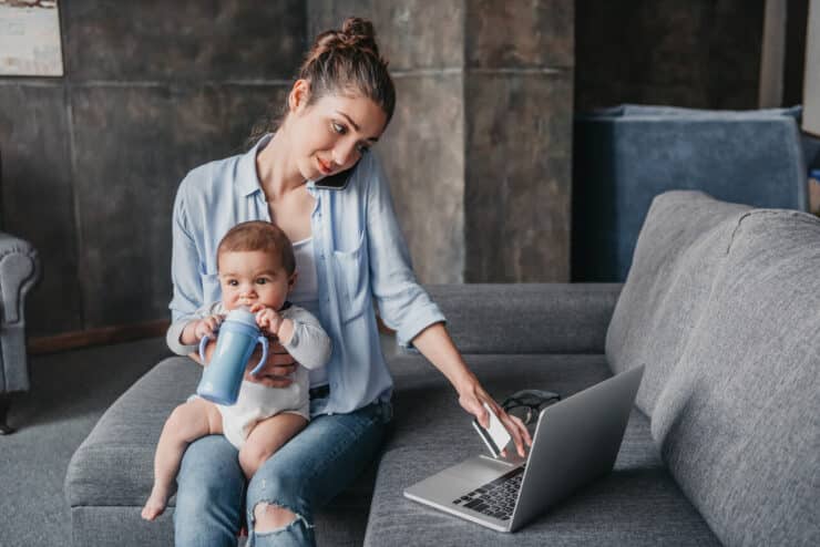 Mama pracująca zdalnie z dzieckiem na kolanach podczas pracy przy laptopie w domu