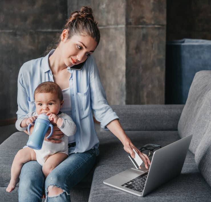 Mama pracująca zdalnie z dzieckiem na kolanach podczas pracy przy laptopie w domu
